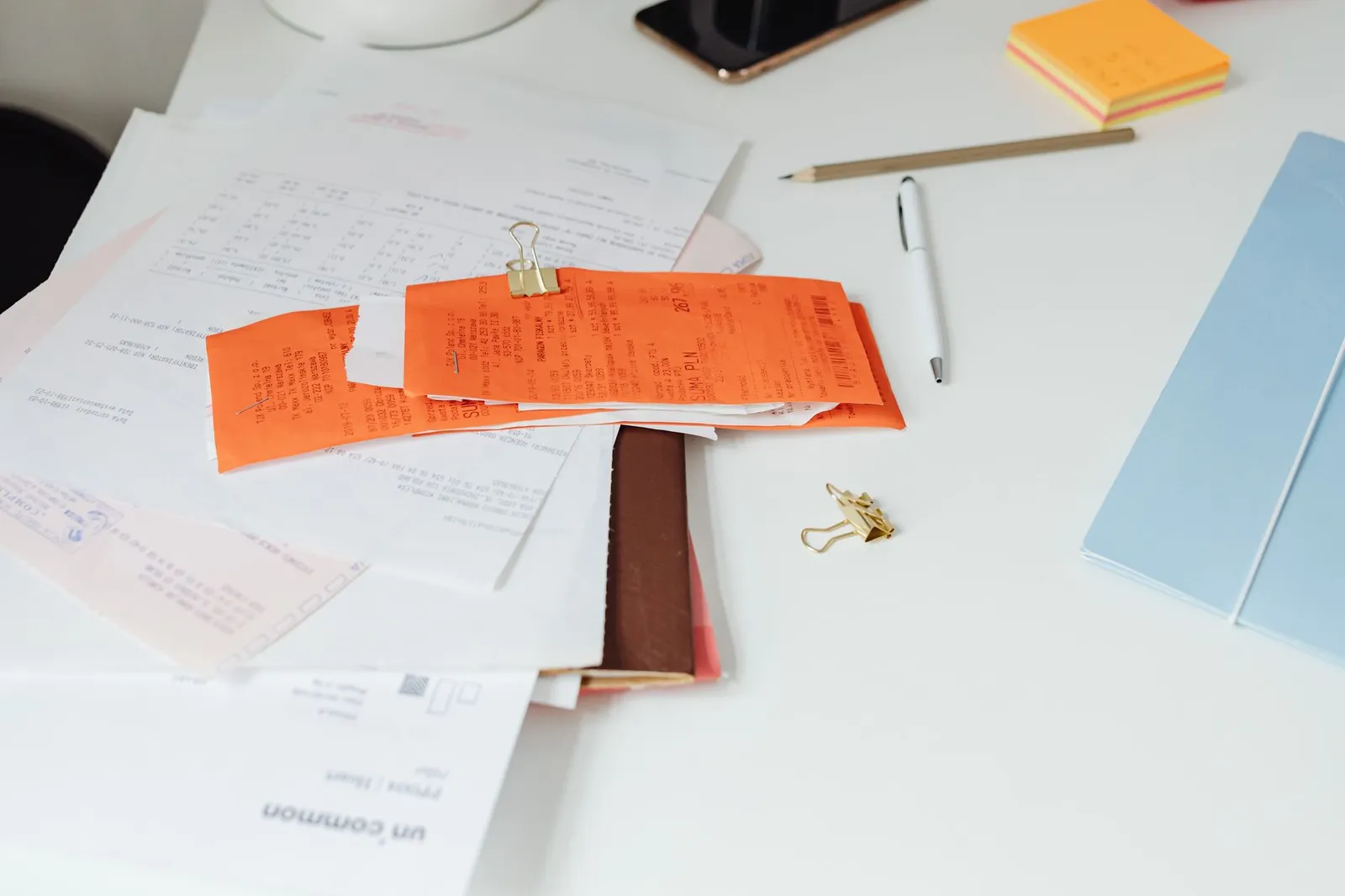 A desk with invoices, a laptop and a notebook of client notes